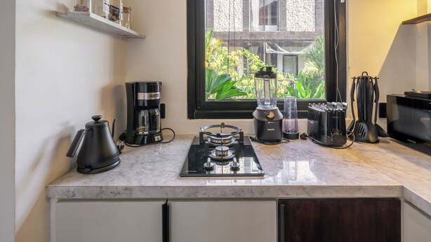 A modern kitchen with a marble countertop, a coffee maker, a blender, and a toaster. - Sebelas Apartments Ubud (Gianyar)