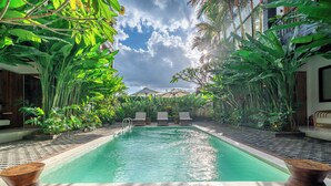 A pool area with lounge chairs and a view of a building in the background. - Sebelas Apartments Ubud (Gianyar)