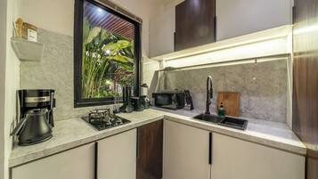 A modern kitchen with a built-in stove, a coffee maker, a sink, and a window with a view of greenery.