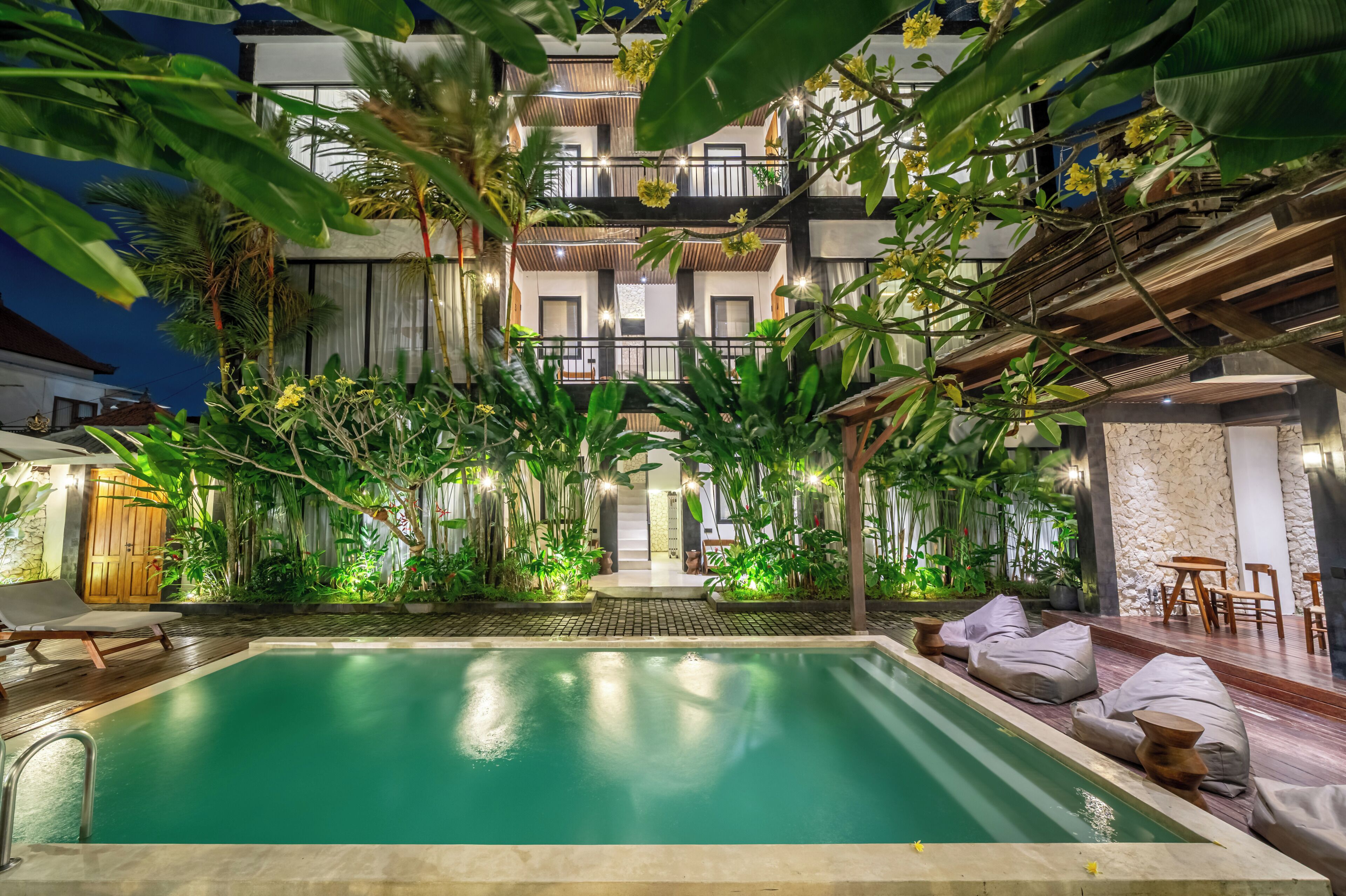 A swimming pool with a surrounding garden, a wooden deck, and a building with balconies.