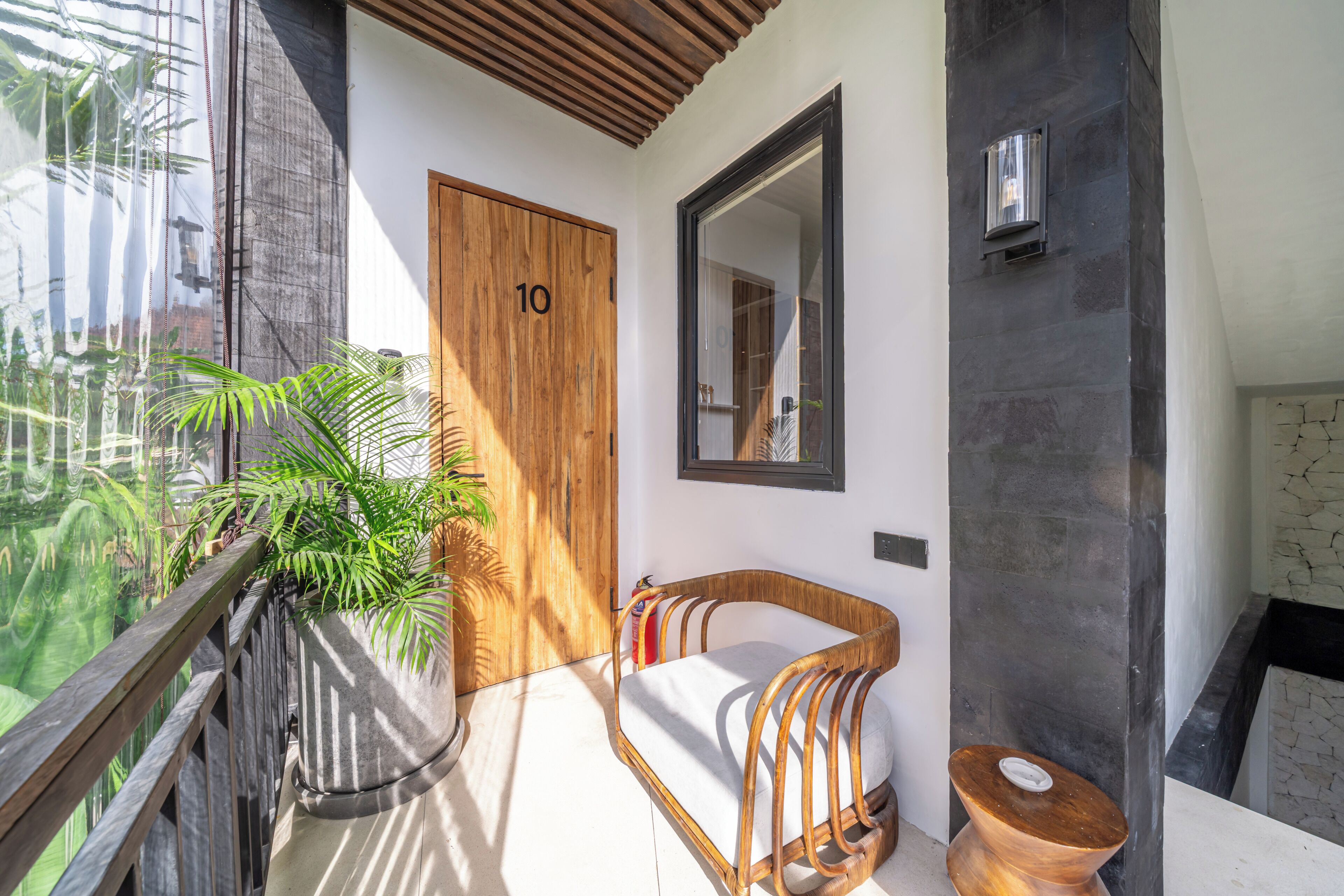 A modern bathroom with a wooden door, a large mirror, a wicker chair, and a toilet.