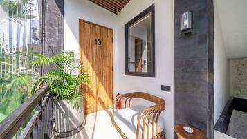 A modern bathroom with a wooden door, a large mirror, a wicker chair, and a toilet.