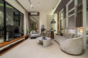 A modern living room with a flat-screen TV, a sofa, a coffee table, and a dining area with a table and chairs.