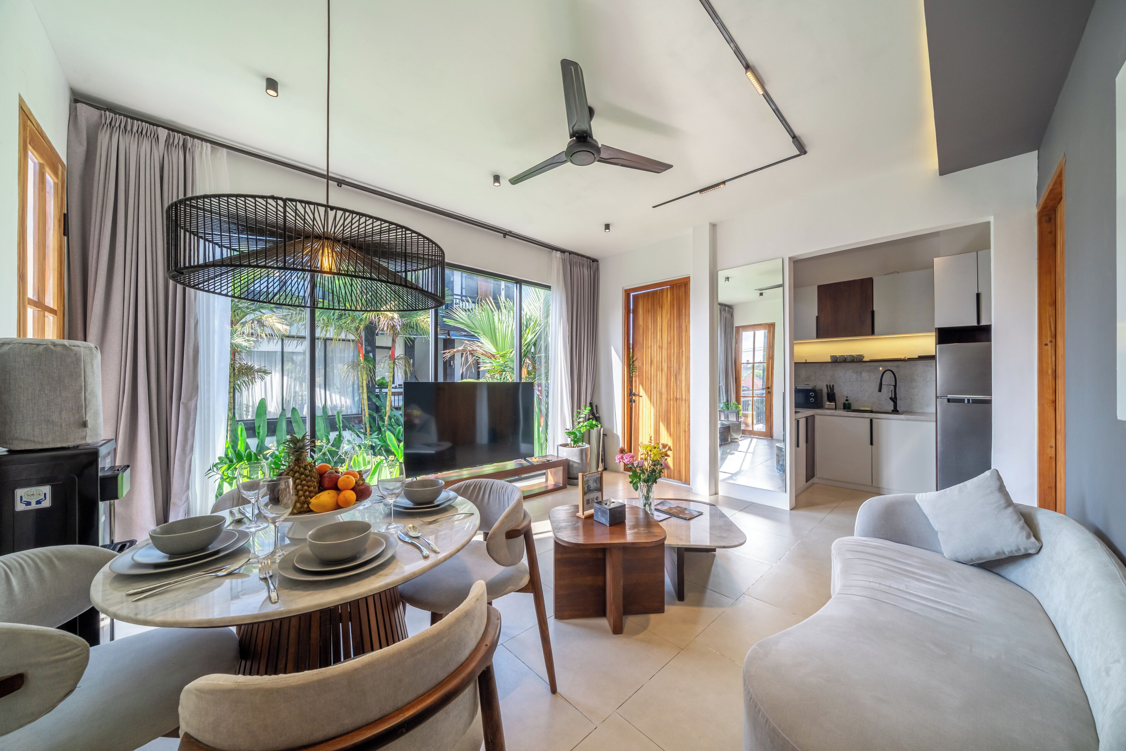 A modern living room with a dining area, a flat-screen TV, and a kitchen visible through an open door.