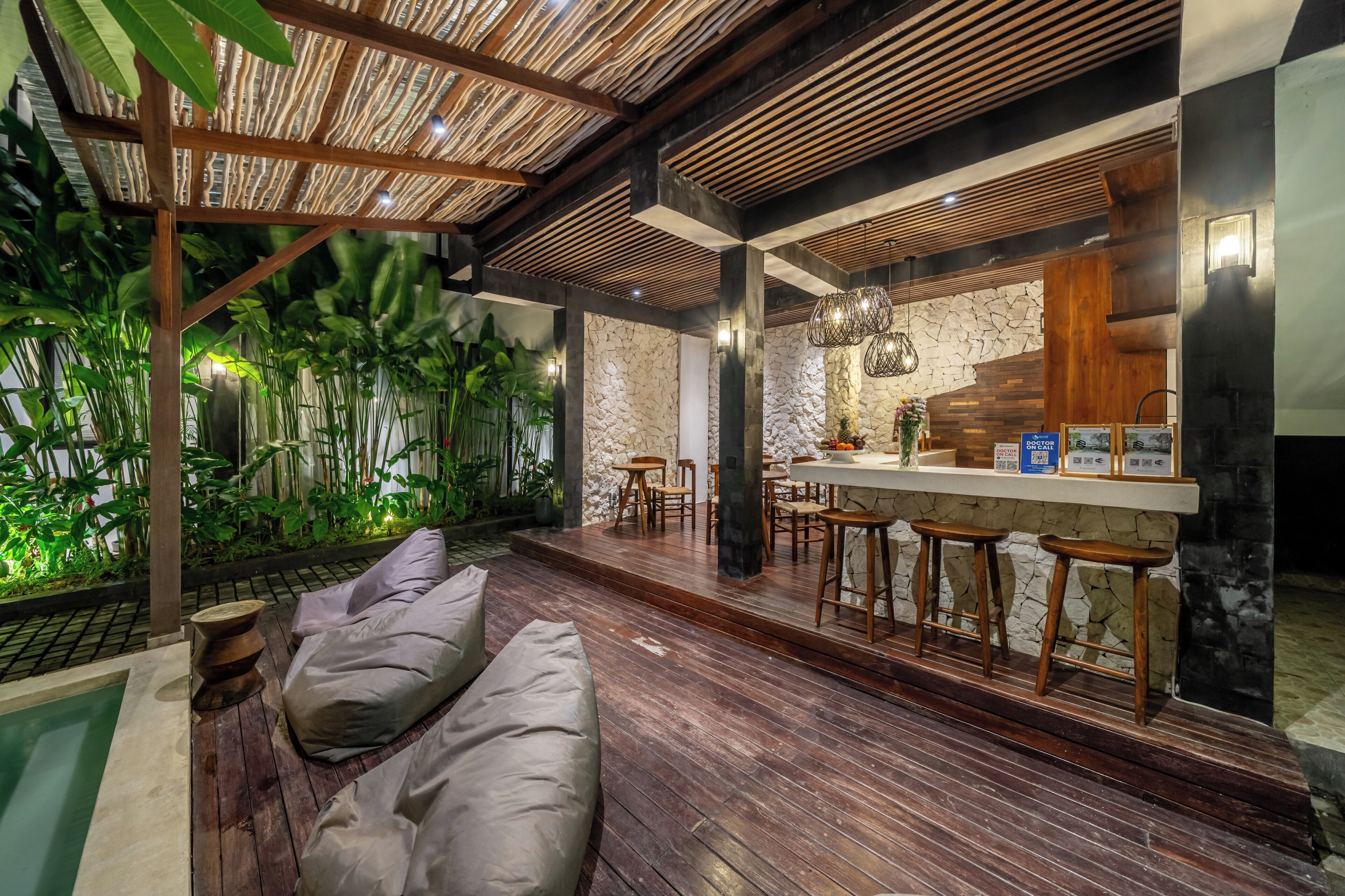 Un interior moderno con suelo de madera, zona de estar con cojines, barra con taburetes y pared de piedra.