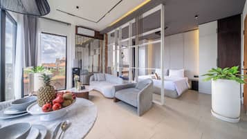 Una habitación de hotel moderna con un ventanal grande, un sofá, una cama y un área de comedor con un frutero.