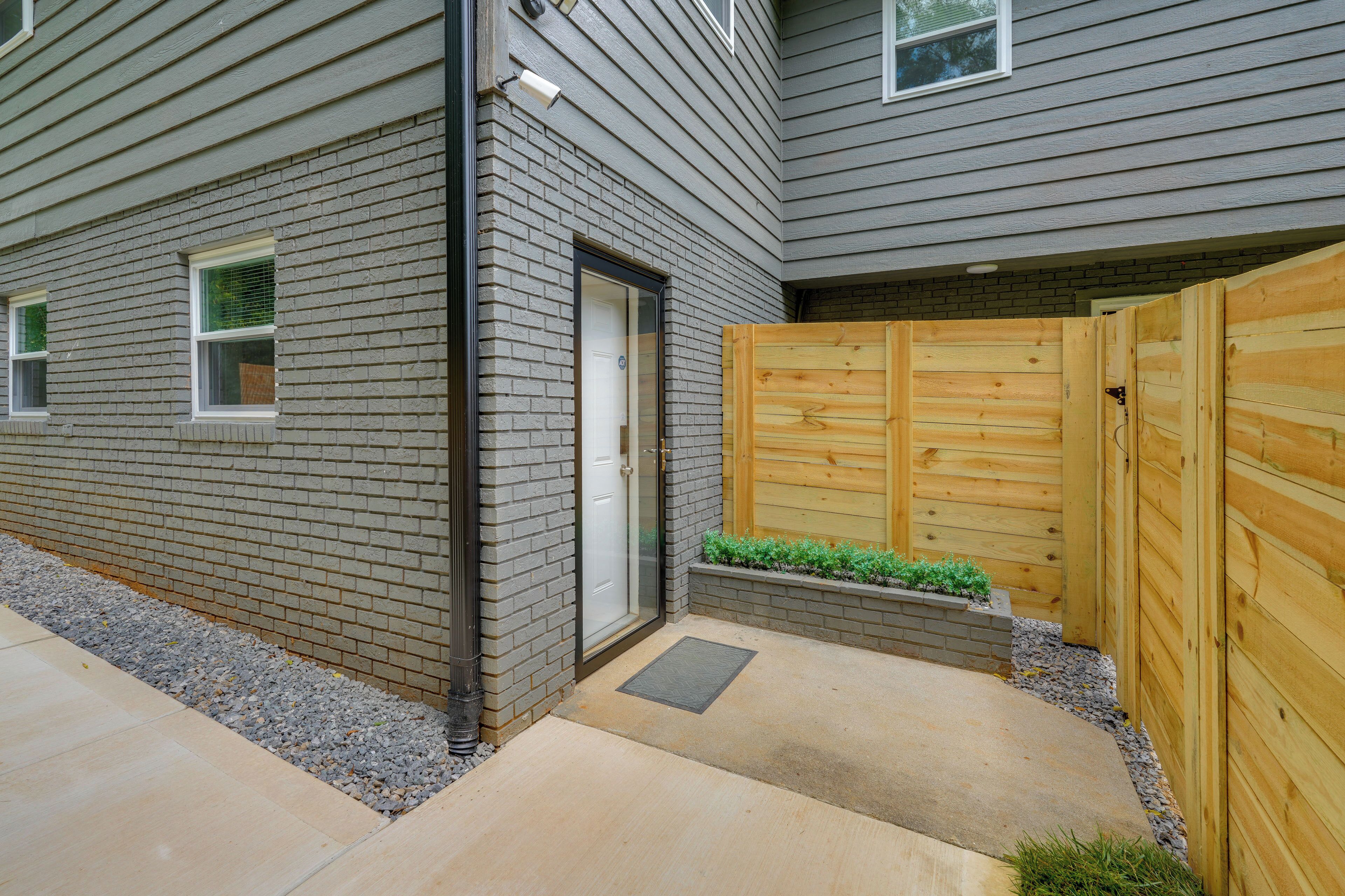 A residential building with a grey siding exterior, a wooden gate, and a small garden area with plants.