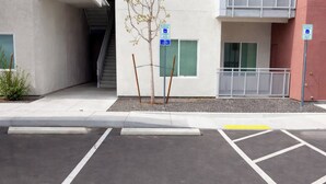 Un espacio de estacionamiento con el símbolo azul para personas con discapacidad, un edificio con rampa y una escalera.