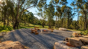 Un espacio al aire libre con bancos y un hogar para fuego, rodeado de rocas y árboles.