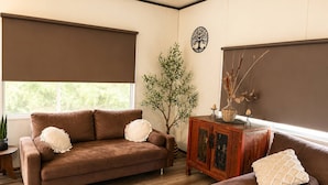 Una sala de estar con un sofá marrón, un sillón a juego, un aparador de madera y una planta decorativa.