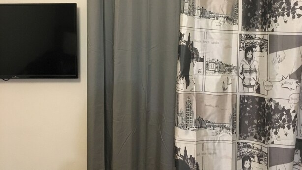 Ett badrum med en grå duschdraperi, en väggmonterad platt-TV och ett vitt element.