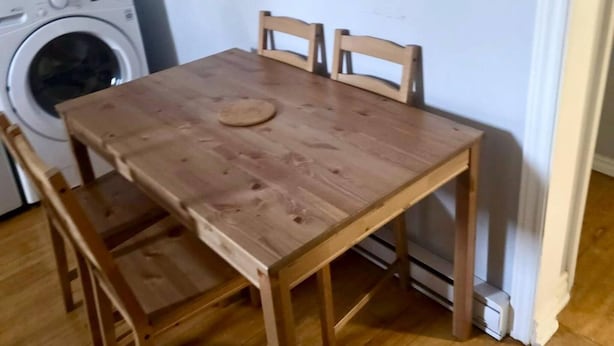 Een klein eetgedeelte met een houten tafel en stoelen, een wasmachine op de achtergrond, en een wandlamp.