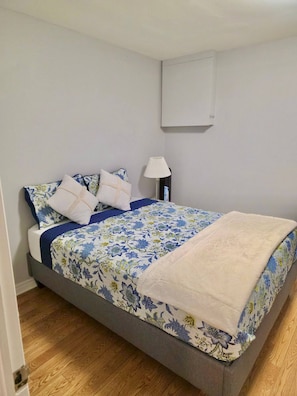 Une chambre à coucher avec un lit, des oreillers, une table de chevet, une lampe et un climatiseur fixé au mur.