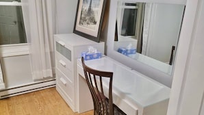 Een kamer met een wit bureau, een stoel, een lijst met een afbeelding en een spiegel.