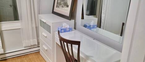 Une pièce avec un bureau blanc, une chaise, un tableau encadré et un miroir.
