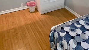 Een slaapkamer met een witte dressoir, een roze prullenbak en een bed met een blauw-witte spreideken.
