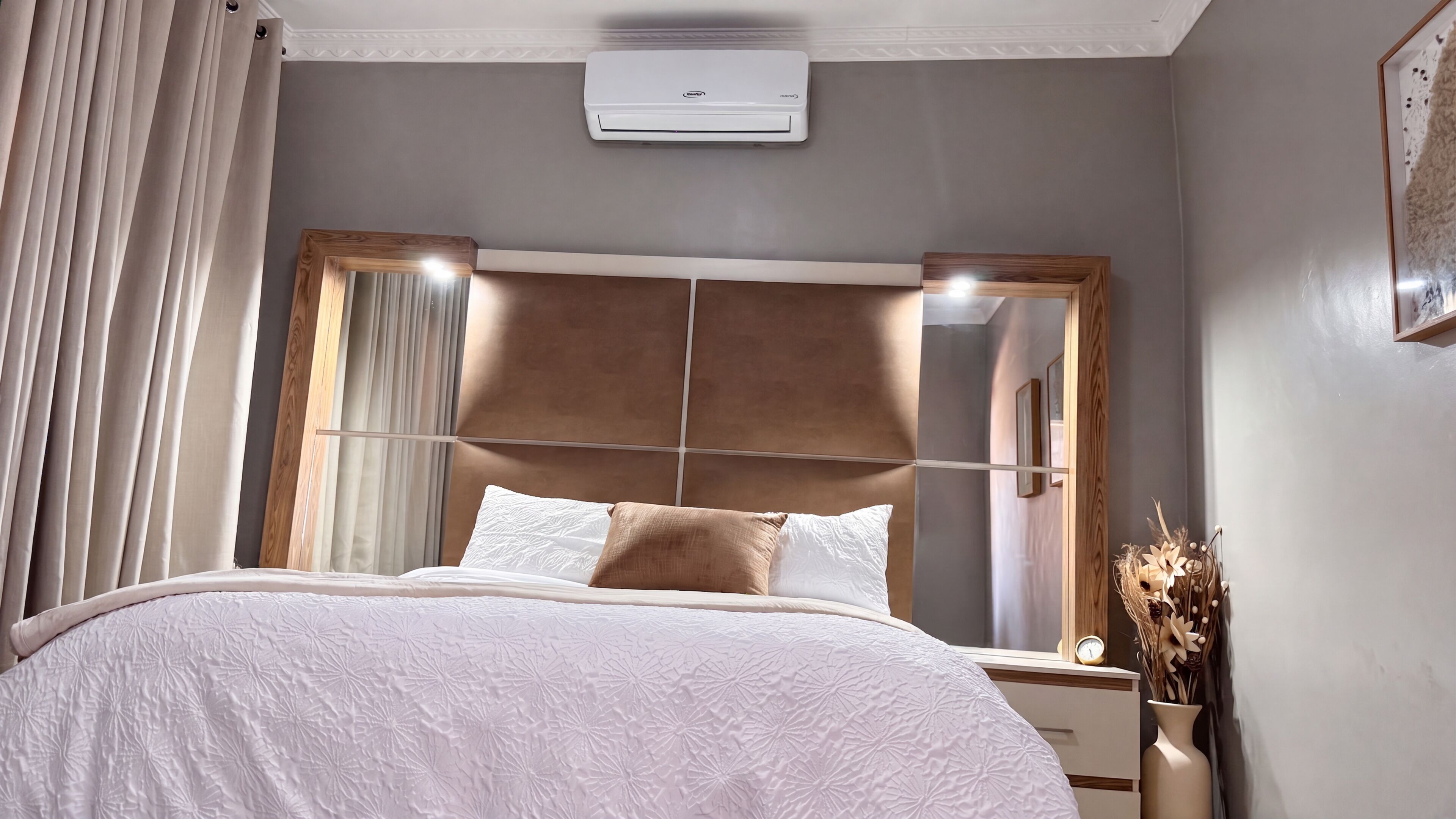 A bedroom with a bed, a nightstand, a wall-mounted air conditioner, and a window with curtains.