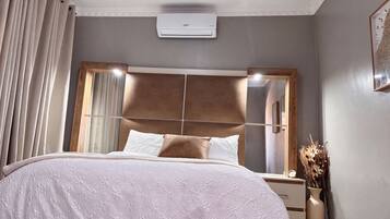 A bedroom with a bed, a nightstand, a wall-mounted air conditioner, and a window with curtains.