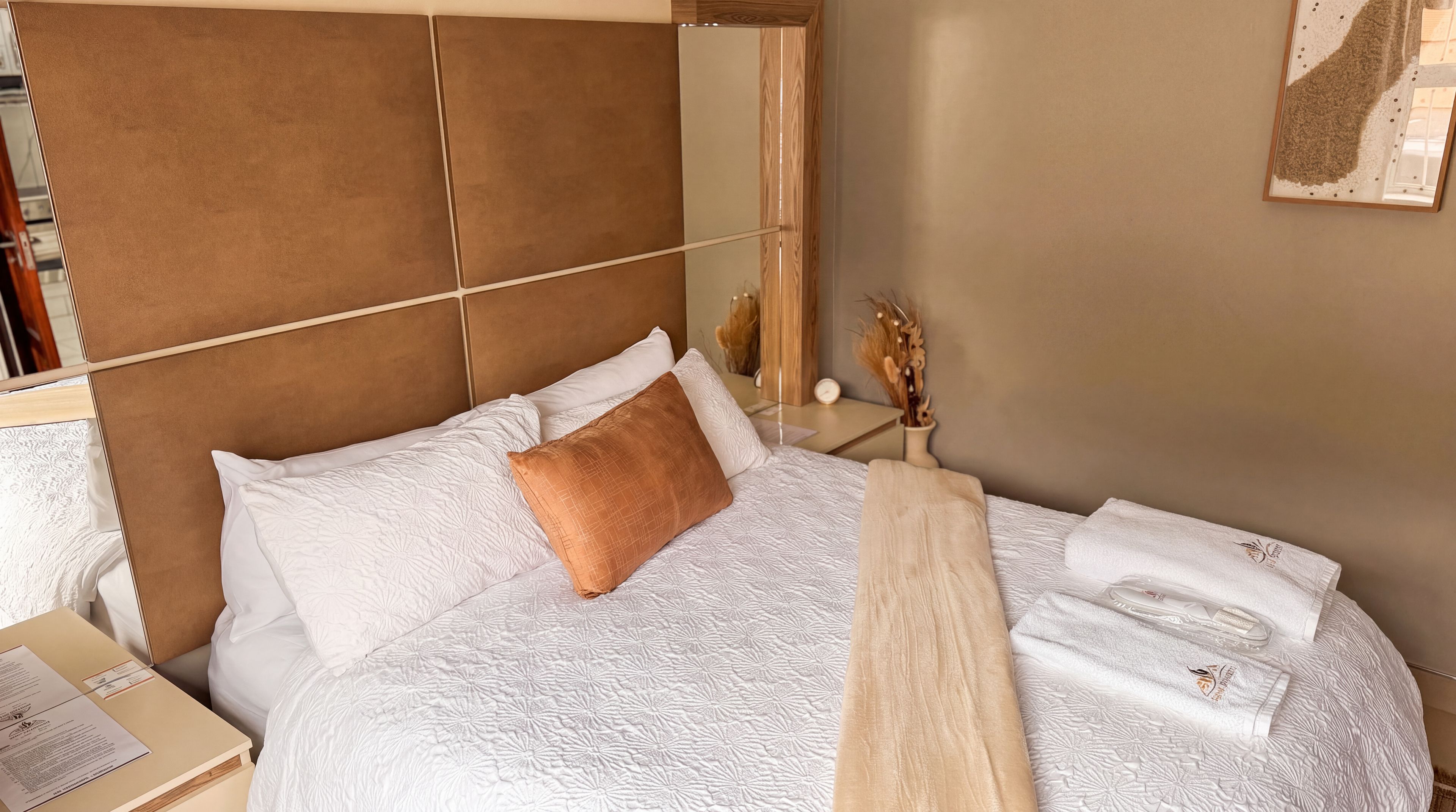 Een netjes opgemaakt bed met hoofdbord, kussens en dekbed.
