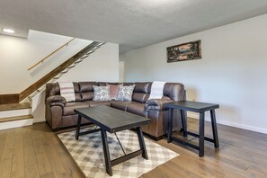 A living room with a brown leather sectional sofa, two black coffee tables, a patterned rug, and a wooden staircase. - Hillside ‘Sunset Vista’ 2 Mi to Dtwn Hughesville (Hughesville)