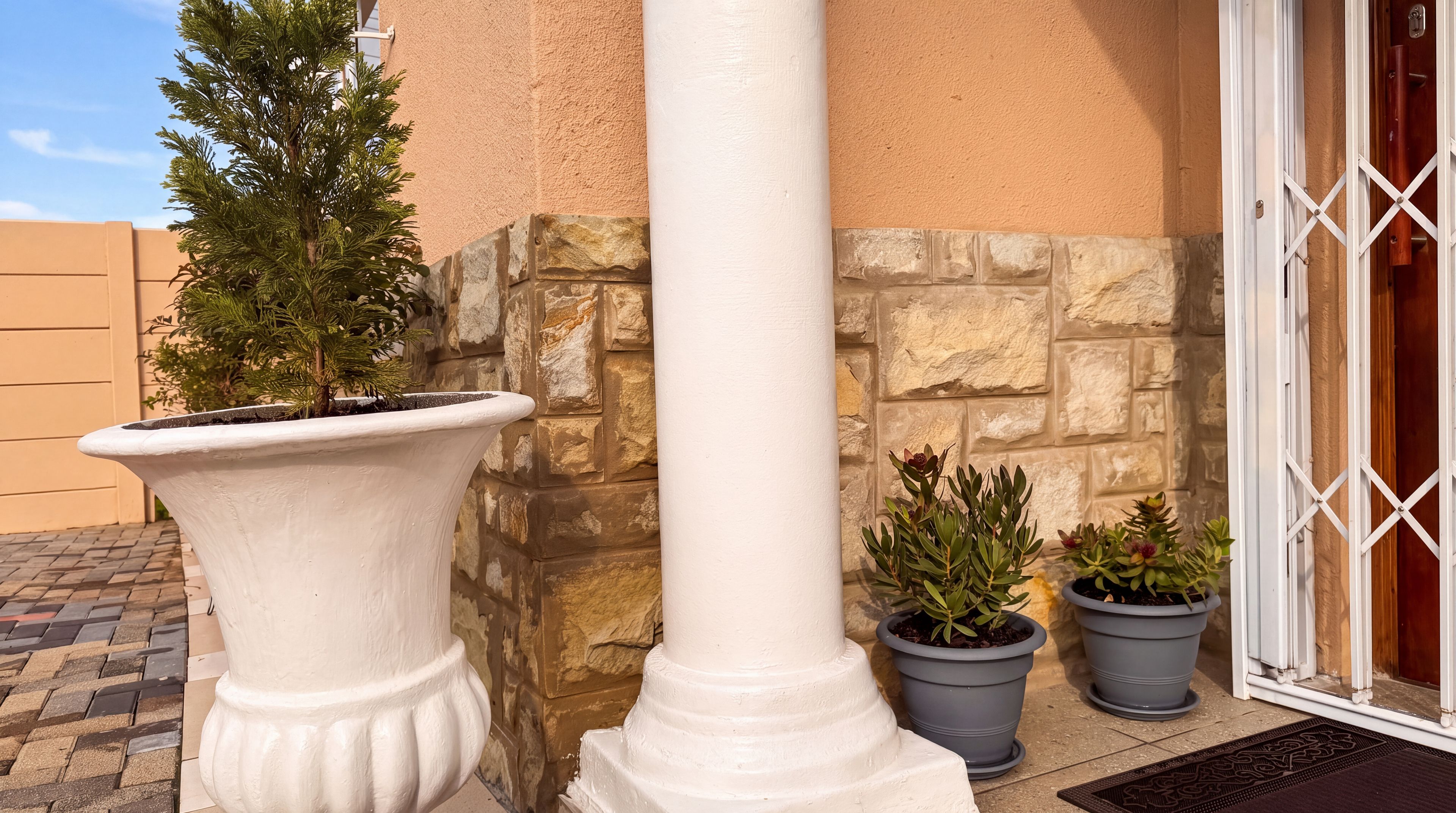 Una esquina de edificio con una columna blanca, una planta en maceta y un muro de piedra.