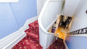 A staircase with red carpet and white balustrade leading to a room with a wooden floor and a patterned rug.