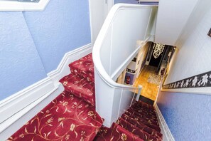 A staircase with red carpet and white balustrade leading to a room with a wooden floor and a patterned rug.