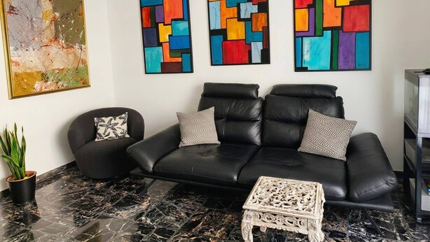 A modern living room with a black leather sofa, two patterned throw pillows, a marble floor, and three abstract paintings on the wall. - Modern Apartment Near Senigallia's Velvet Beach (Senigallia)