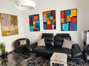 A modern living room with a black leather sofa, two patterned throw pillows, a marble floor, and three abstract paintings on the wall. - Modern Apartment Near Senigallia's Velvet Beach (Senigallia)