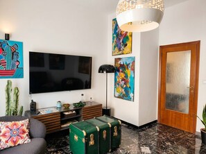 Un salon équipé d’un téléviseur à écran plat, d’une lampe moderne, d’un canapé, d’une table basse et d’une malle verte.