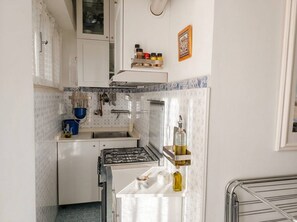 A compact kitchen with white cabinets, a gas stove, a sink, and a spice rack. - Modern Apartment Near Senigallia's Velvet Beach (Senigallia)