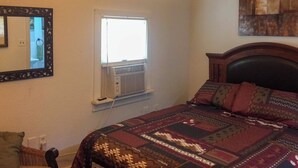 Une chambre à coucher comprenant un lit, une fenêtre avec un appareil de climatisation, un miroir et une œuvre d’art accrochée au mur.
