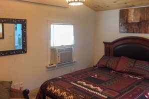 Ein Schlafzimmer mit einem Bett, einem Fenster mit Klimaanlage, einem Spiegel und einem Wandbild.
