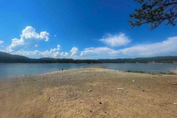 Une vue sur le lac, avec une rive de galets, une eau calme et des collines à l’horizon.