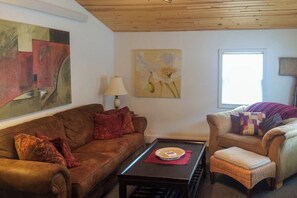 Ein Wohnzimmer mit einem braunen Sofa, einem Korbstuhl, einem Couchtisch und Kunstwerken an den Wänden.