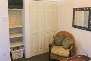 A room with a closed white closet, a wicker chair with cushions, a wicker basket, and a mirror on the wall. - Charming Home on Main Street in Deadwood! (Deadwood)