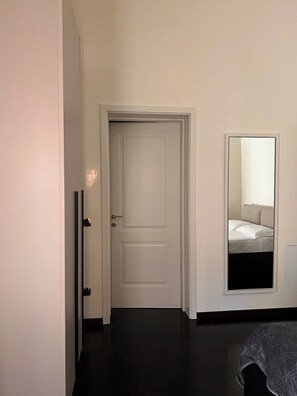Ein Zimmer mit geschlossener Tür, einem Bett mit weißer Bettwäsche und einem Spiegel an der Wand.