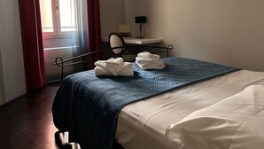 Ein Hotelzimmer mit einem Bett, einem Schreibtisch mit Lampe und einem fenster mit Vorhängen.