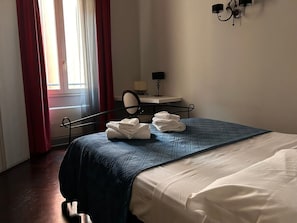 Ein Hotelzimmer mit einem Bett, einem Schreibtisch mit Lampe und einem fenster mit Vorhängen.