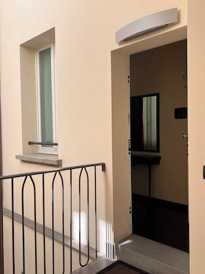 Um corredor com uma porta que dá para um quarto, uma janela com vista e um corrimão de metal.