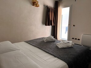 Una habitación de hotel con una cama, una ventana con cortinas, un aire acondicionado de pared y un termostato.