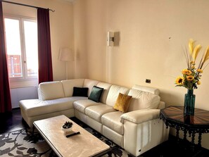 Ein Wohnzimmer mit einer Couch, einem Couchtisch, einer Vase mit Blumen, einer Lampe und einem Fenster mit Vorhängen.