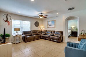 A living room with a sectional sofa, a ceiling fan, a clock, and a painting on the wall. - Pet-Friendly Cape Coral Home w/ Pool & Hot Tub (Cape Coral)