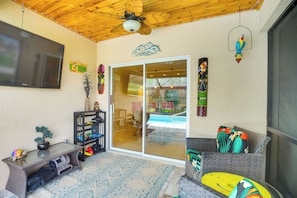 Ein Zimmer mit Deckenventilator, Fernseher, Glastür zum Außenbereich und verschiedenen Dekorationselementen, darunter eine Papageienskulptur und ein Schild.