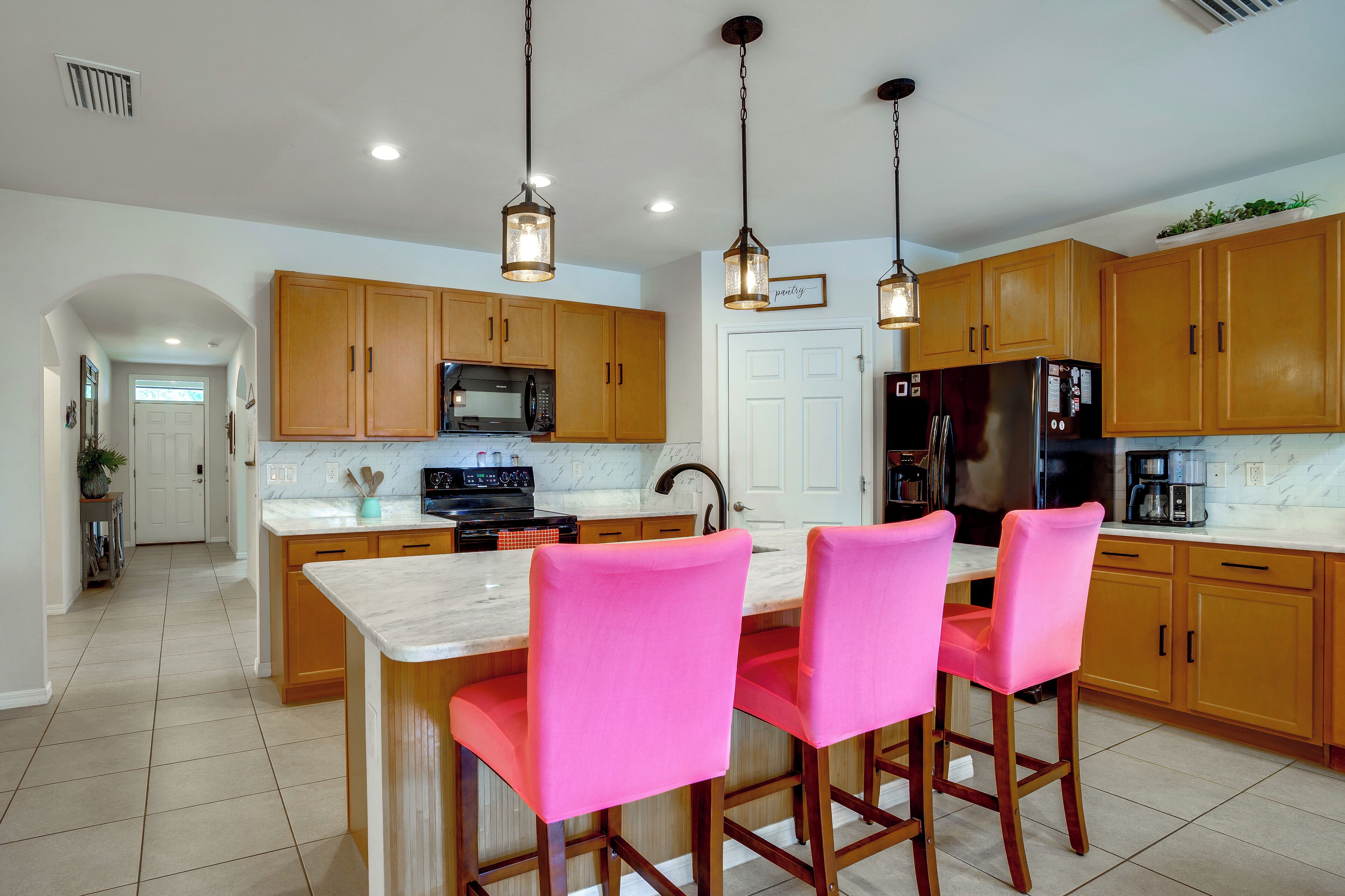 A kitchen with wooden cabinets, a marble countertop, a stainless steel refrigerator, and a bright pendant light.