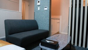 Habitación de hotel con un sofá azul oscuro, una mesita redonda y una caja de pañuelos, además de un armario blanco.