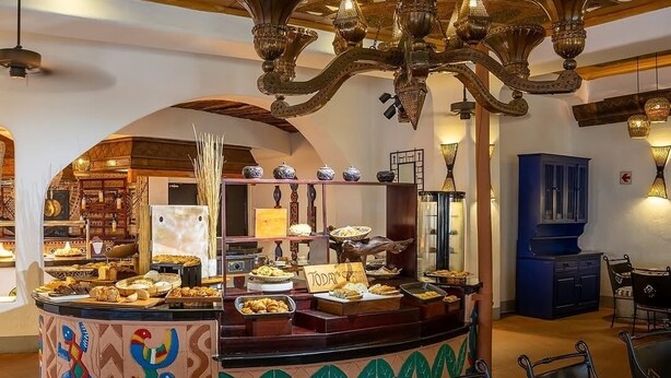 A buffet area with a variety of food items, a chandelier, and a seating area with tables and chairs.