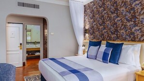 A hotel room with a large bed, a bathroom with a mirror, and a patterned wall.