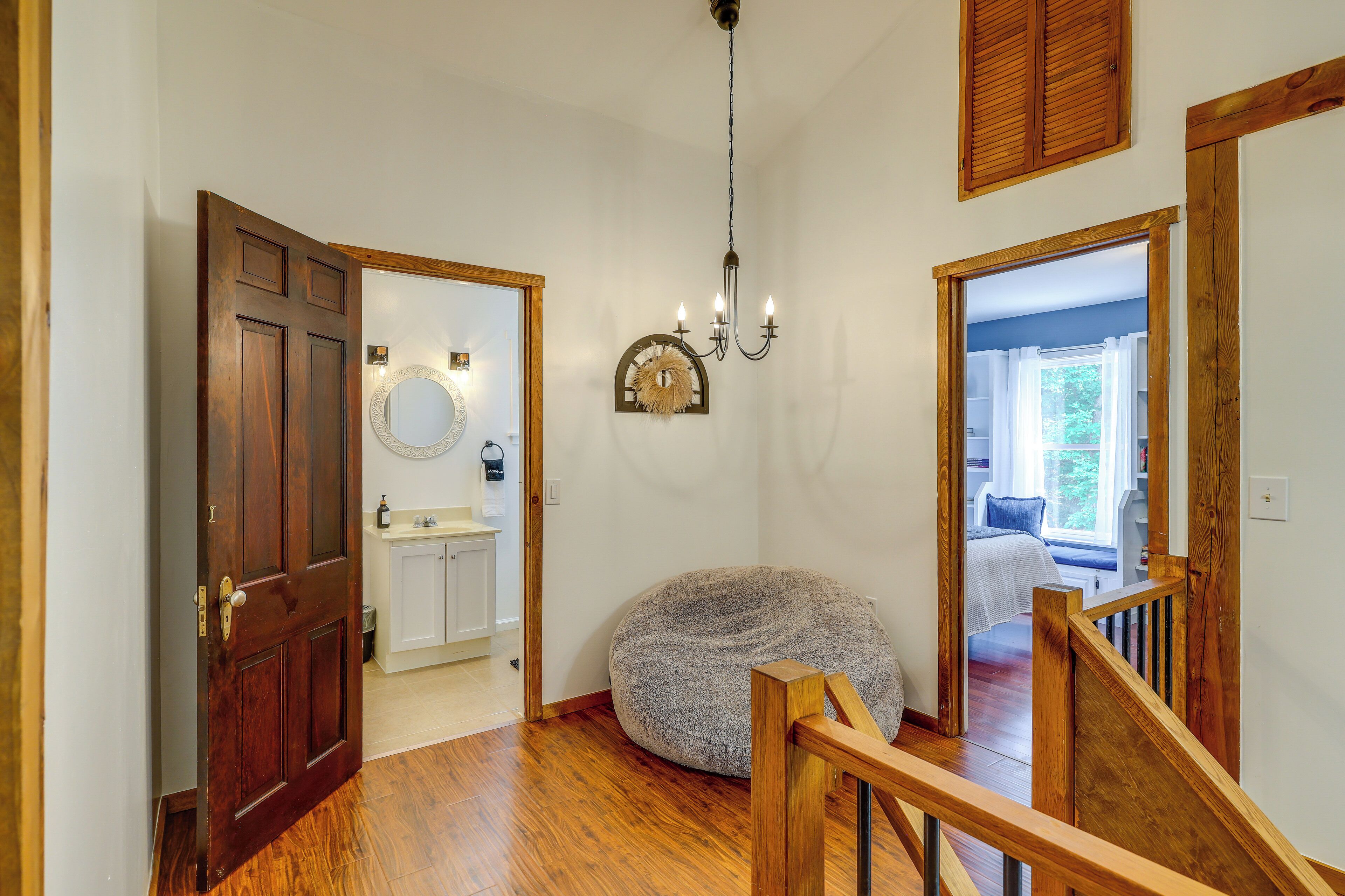 A hallway with a wooden door, a round mirror, a chandelier, and a round bean bag chair.