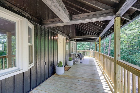 A covered porch with a wooden railing, a bench, and potted plants.